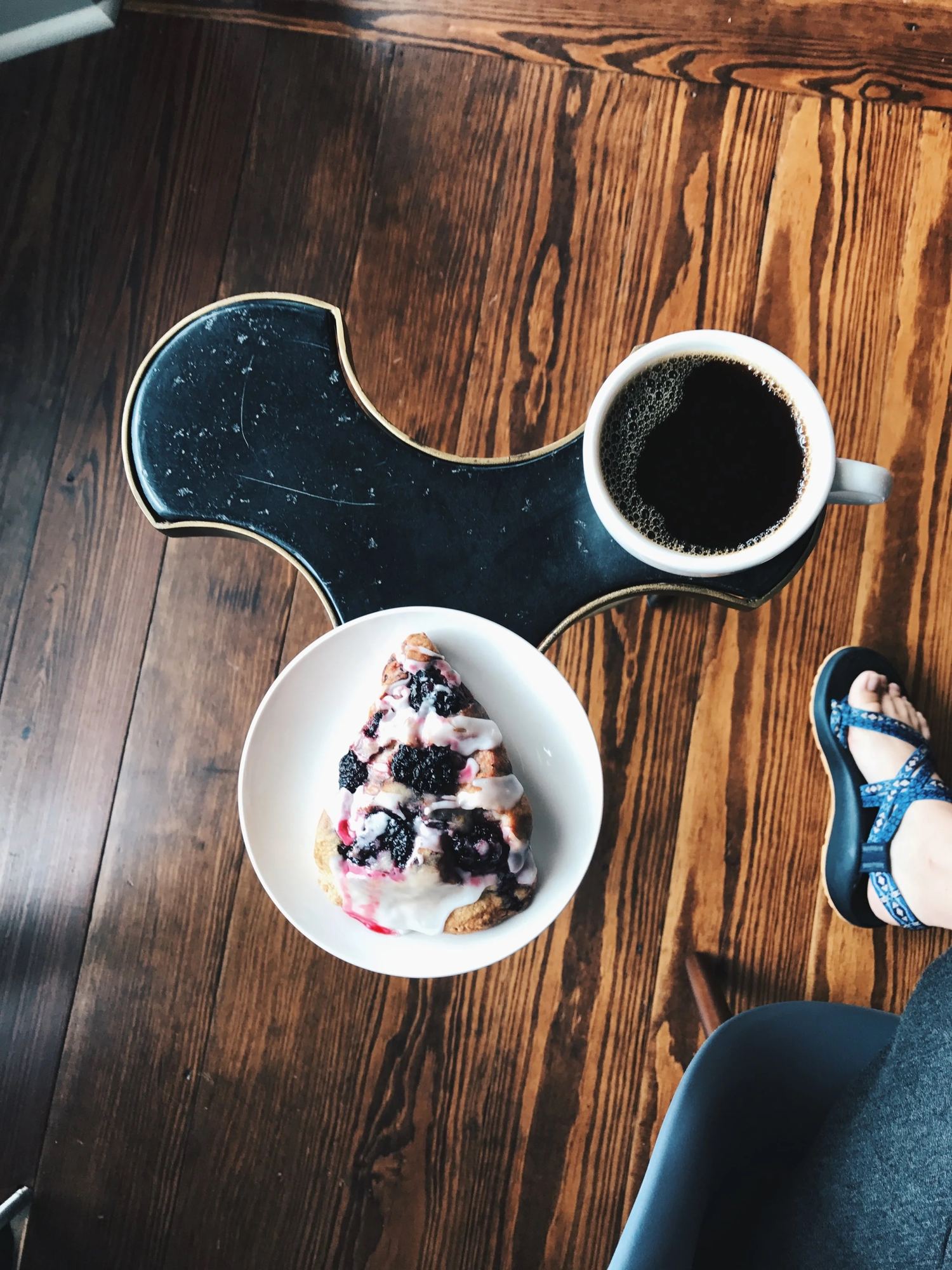 A blueberry pastry and a black coffee on a wooden table