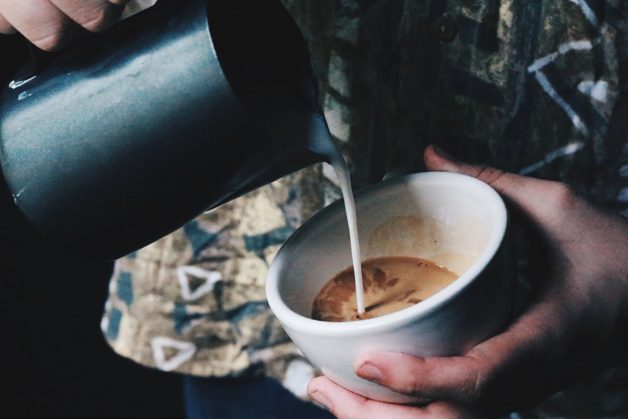 A barista pouring steamed milk into a cup