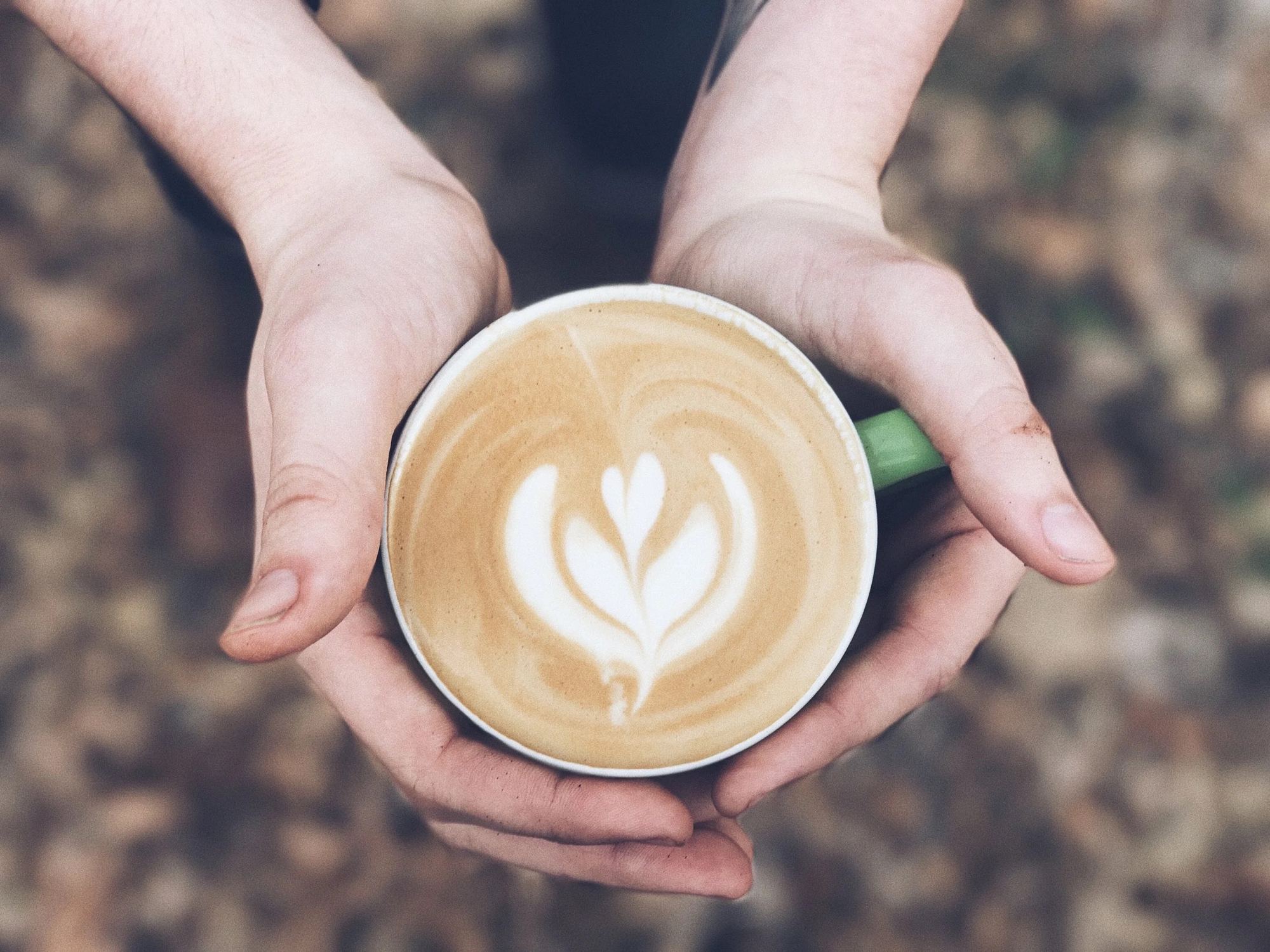 Two hands around a latte with a heart poured in the foam