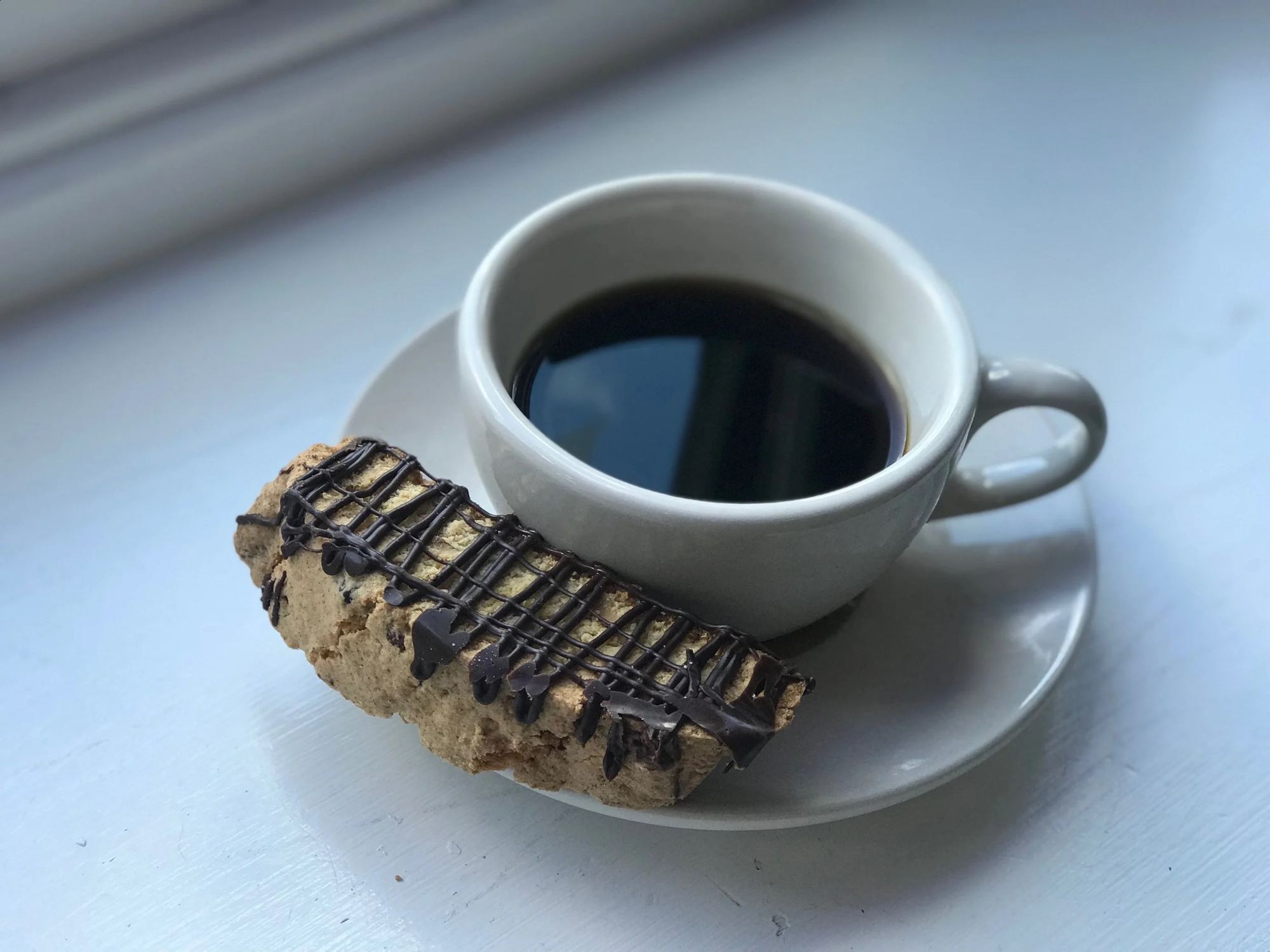 A cup of black coffee with chocolate-drizzled biscotti